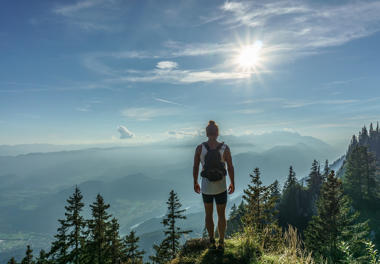 Escursionista in cima a una montagna con vista panoramica mozzafiato su un paesaggio naturale.