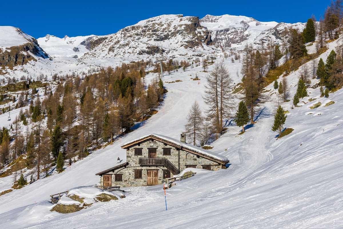 Rifugio di montagna panoramico in Italia circondato da vette e boschi verdi.